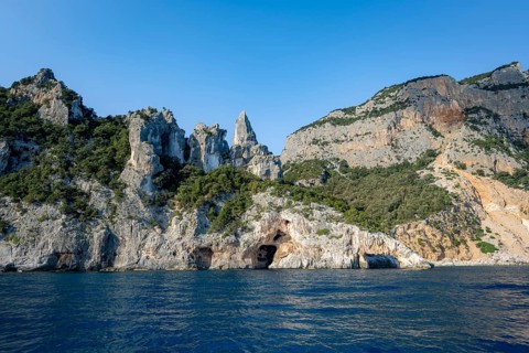 Picturesque rocky coast, cliffs with caves in the morning light, L'Aguglia rock peak, blue sea and
