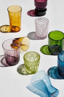 From above a collection of colorful, textured glassware arranged artfully on a white surface,