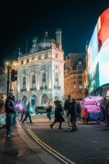 Glowing city at night, buildings illuminated by lights, people and billboards, New Year's Eve