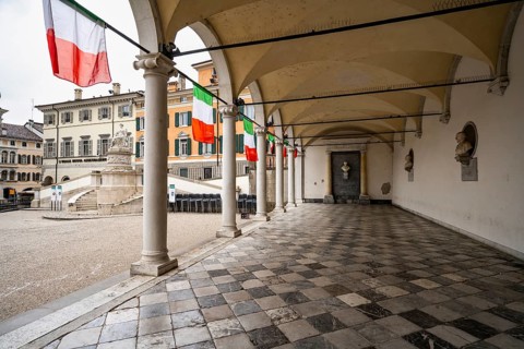 Corridor of the Loggia e Tempietto di San Giovanni with Italian flags, main square Piazza della