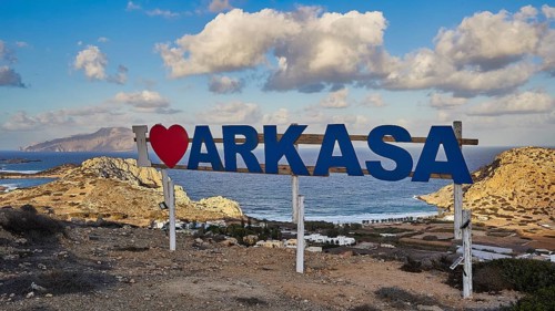 Town sign 'I love Arkasa' in front of rocky coast under cloudy sky, Arkasa, west coast, Karpathos,