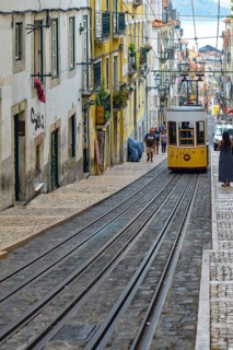 A yellow tram descends a steep, narrow alleyway full of charm in an urban setting, Lisbon, Portugal