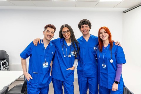 Diverse group of smiling medical students in blue scrubs with stethoscopes, arms around shoulders,