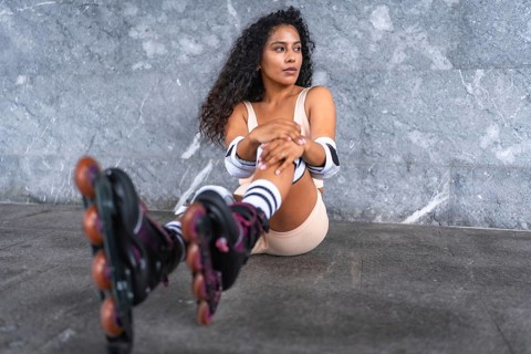 Portrait of a young latin woman with long curly hair wearing in-line skates sitting outdoors
