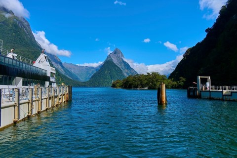 Calm fjord with steep mountains in the background, boats anchored at the pier under a clear sky,