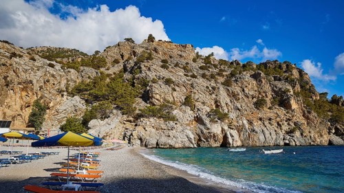 Rocky coastline with a beach full of parasols on a clear, sunny day, Ahata Beach, Ahata, East