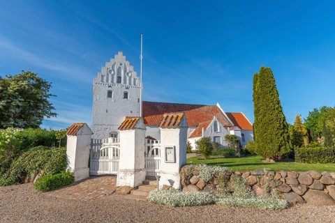 Whitewashed church in Dalby, side view, red roof, cemetery, stepped gable, entrance gate, stone