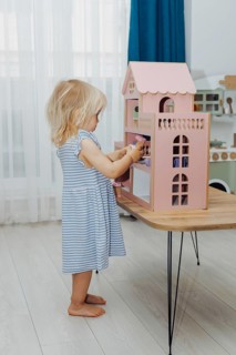 Blonde Toddler Girl playing with pink doll house in children room