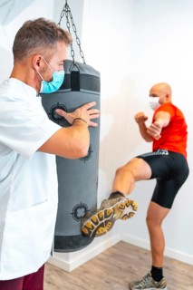 Physiotherapist with mask together with the patient on the punching bag. Physiotherapy with