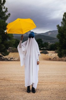 Playful ghost walking with a yellow umbrella outdoors during Halloween season. Creative homemade