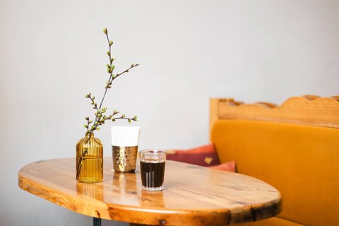 A cozy cafe scene featuring a wooden table with a glass of coffee, a textured cup, and a simple