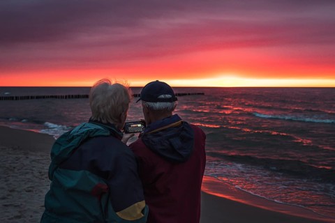 Couple old people with smartphone during sunset by the sea