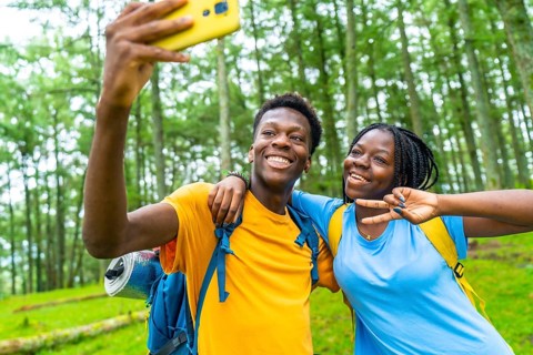 Happy young african friends gesturing success while taking selfie together in a green forest