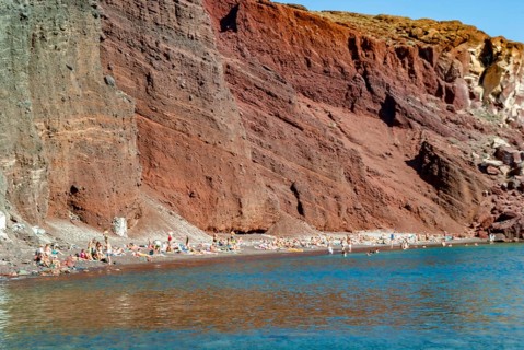 Tourists on the shores of the Red Beach in Santorini, A sunny day at a beach with red cliffs and