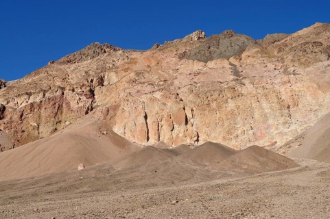 Erosion-shaped rock cliffs rise above a sandy desert landscape under clear skies, Artist Drive,