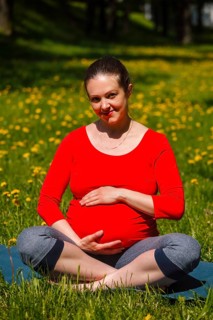Pregnancy yoga exercise, pregnant woman doing asana Sukhasana easy yoga pose holding her abdomen