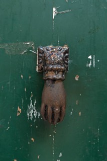 Hand as a door knocker on a front door in the historic centre, Genoa, Italy