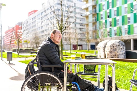 Young man in a wheelchair enjoys a beverage with a friend at an outdoor cafe, embracing urban life