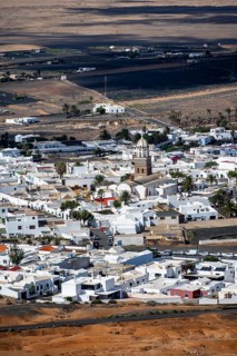 View of town, white houses of Teguise with church tower in dry volcanic landscape, Lanzarote,