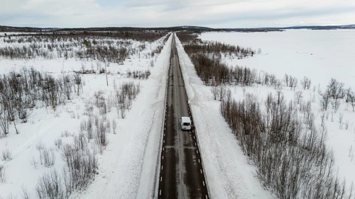 Aerial view of a long, straight road cutting through a snow-covered landscape, lined with sparse
