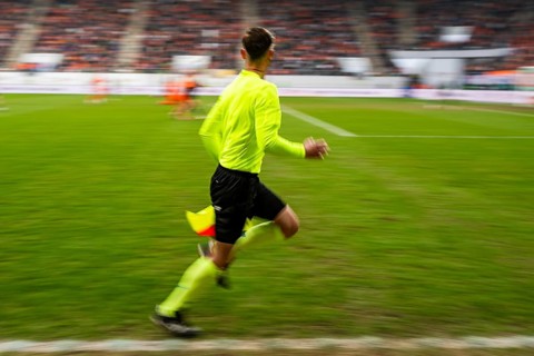 Assistant referee in a vibrant neon yellow kit running along the sideline during a professional