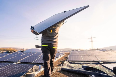 A worker carries a solar panel on a roof under bright sunlight, PV installation at OBI Baumarkt,
