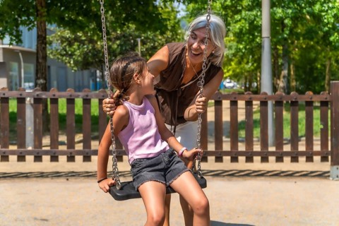 Granddaughter enjoying a fun swing ride at a park playground as her happy grandmother pushes the