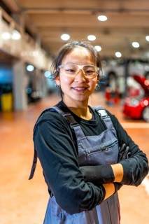 Confident female mechanic wearing protective glasses and earplugs, smiling with arms crossed in a