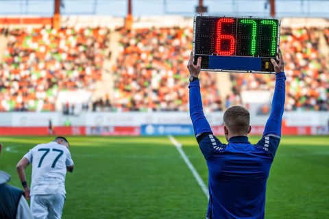 Rear view of a fourth official holding an electronic substitution board showing numbers 6 and 77 at