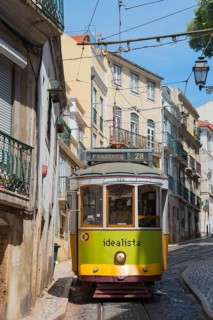 A yellow-green tram runs along a steep alley with old buildings in the background, Tram, Line 28,
