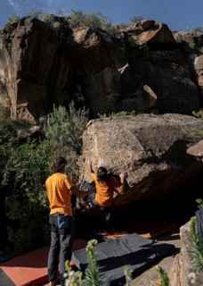 Two climbers tackle a challenging boulder problem in a picturesque natural setting, showcasing
