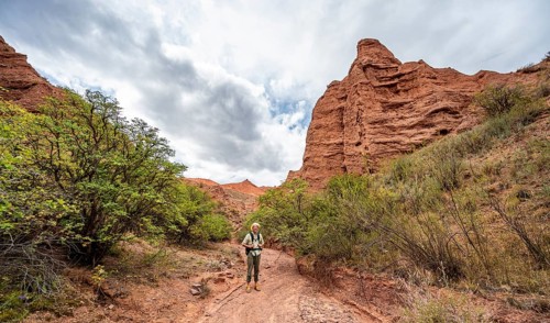Mountaineer in a canyon with a dry stream bed, eroded mountain landscape with red sandstone rocks,
