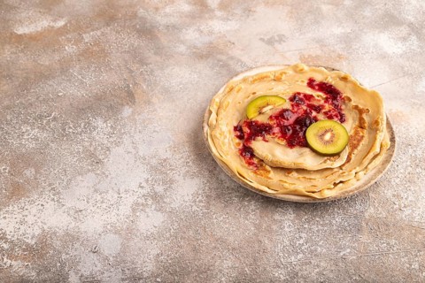 Stack of Plain Fried pancakes with jam and kiwi on brown concrete. side view, copy space