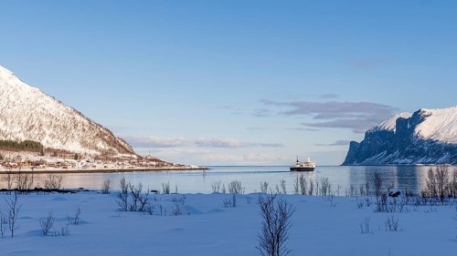 A tranquil winter scene in Norway captures a ferry gliding across a calm fjord, framed by