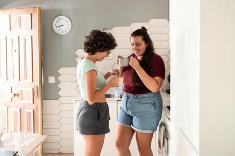 A loving lesbian couple enjoys a morning coffee together in their modern kitchen. They share smiles