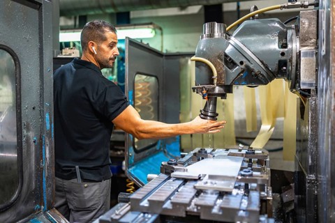 Three quarter length side view of a caucasian male worker using milling machine in a cnc factory