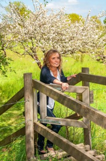 Young smiling woman opening a gate in a fence and with a blooming apple tree in the background in