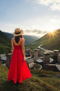 Young pretty Woman traveler in red dress looking at medieval towers of Ushguli Georgia during