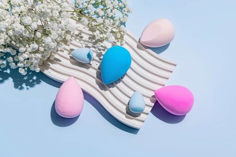 Top view of vibrant makeup sponges arranged aesthetically on a textured, wavy surface alongside