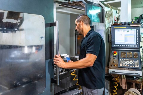 Rear side view of a male caucasian adult technician using milling machine commands in a cnc factory