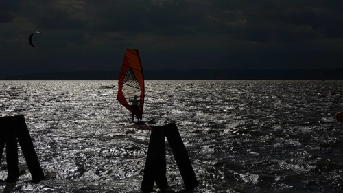 A surfer silhouette in moonlight on a dark, wavy lake, Lake Neusiedl, Austria