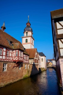 Half-timbered houses and a church on a river under a blue sky in a historic old town, Mümling