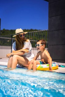 Vertical photo of a caucasian mother and boy with rubber ring sitting on a swimming pool together