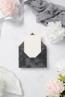 A chic wedding stationery arrangement featuring a blank card in a dark envelope, surrounded by