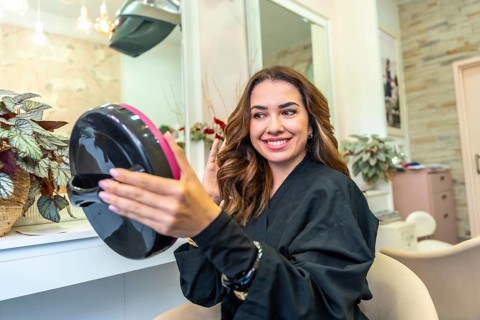 Woman wearing a black gown smiling with satisfaction, looking in a small hand mirror at her newly