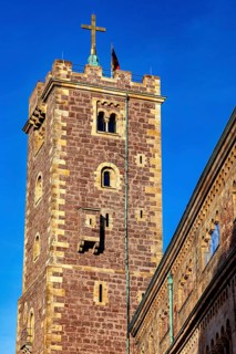 Close-up of a tower with a cross on the roof, surrounded by a historic stone building, The Wartburg