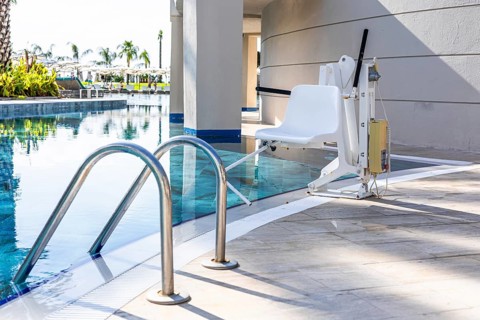 A poolside lift chair for disability people is positioned next to a swimming pool. The area is