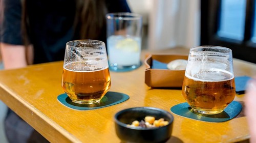 A cozy restaurant table with two beers and a lemon drink, accompanied by a dish of mixed nuts,