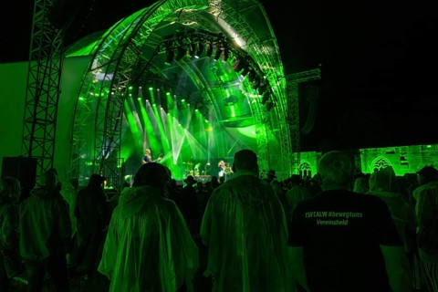 People in rain ponchos and a T-shirt in the crowd at a night concert with green stage lighting,