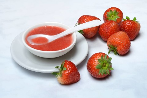 Strawberry sauce in small bowls and strawberries, strawberry coulis